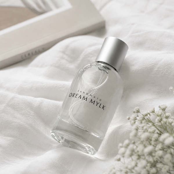 Clear bottle of 'Dream Mylk' on a white fabric background with flowers.